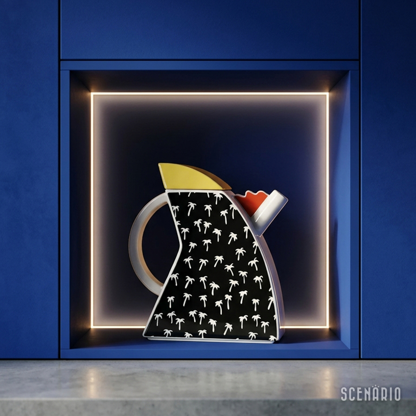 caffettiera-memphis-ambientata-cucina-blu-cobalto.jpg Vista frontale ravvicinata della caffettiera Memphis-style di Studio Lampo, posizionata all'interno di una nicchia illuminata a LED a livello dei pensili di una cucina moderna. L'arredamento della cucina è in blu cobalto opaco e la nicchia ha un ripiano in cemento lucido. L'ambientazione evidenzia il contrasto tra la ceramica grafica a palme della caffettiera e il colore profondo dei mobili.
